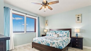 Un dormitorio con una cama de madera, dos mesitas de noche, un ventilador de techo y una ventana con persianas.
