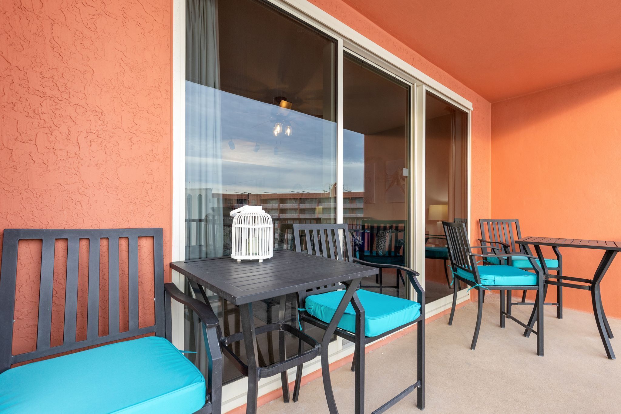 A balcony with a table and chairs, a white birdcage, and a view of the sky through a glass door.