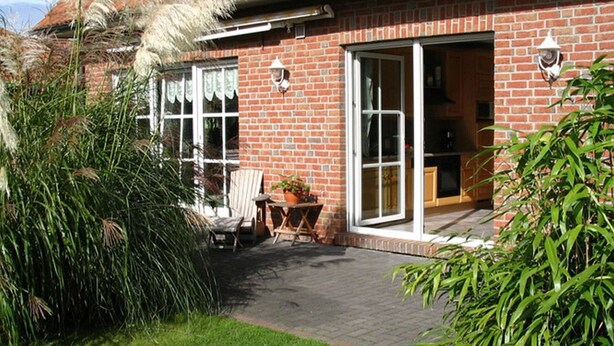 A brick house with a patio, a chair, a table, and a potted plant.
