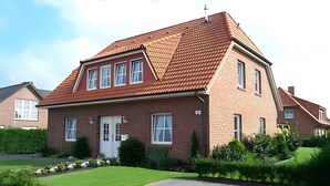 A two-story house with a red-tiled roof, a brick facade, and a front door with a small porch.