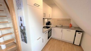 A kitchen with white cabinets, a wooden staircase, and a tiled backsplash.
