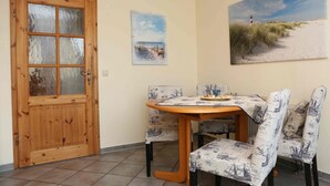A dining area with a wooden table and chairs, a painting of a beach scene, and a wooden door. - Apartment Martina Hans 3 with Terrace and Garden (Horumersiel)