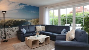 A living room with a sectional sofa, a coffee table, and a mural of a beach scene. - Apartment Martina Hans 3 with Terrace and Garden (Horumersiel)