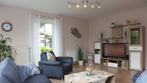 A living room with a sofa, armchair, coffee table, TV, and a window with curtains. - Apartment Martina Hans 3 with Terrace and Garden (Horumersiel)
