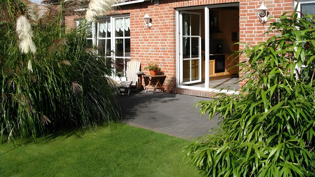 A brick house with a patio, a dining area, and a garden with various plants. - Apartment Martina Hans 3 with Terrace and Garden (Horumersiel)