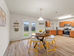 A modern kitchen with wooden cabinets, a stainless steel oven, and a dining area with a round table and yellow chairs. - Warm Cozy 3BR/2BA Fort Worth NRH Home - Cul-de-Sac (Fort Worth)