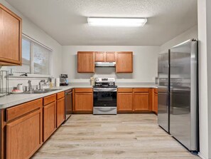 A modern kitchen with wooden cabinets, stainless steel appliances, and a light wood floor. - Warm Cozy 3BR/2BA Fort Worth NRH Home - Cul-de-Sac (Fort Worth)