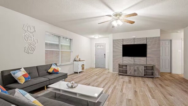 Een moderne woonkamer met een grijze bank, een witte salontafel en een houten tv-meubel met een flatscreen televisie.
