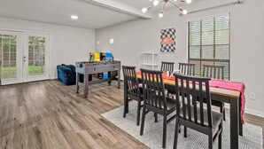 A spacious room with a dining table, chairs, a foosball table, and a ceiling fan. - 4BR Home w/ Arcade, Foosball & Desks - Carrollton (Carrollton)