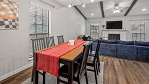 A modern living room with a fireplace, a dining area with a red tablecloth, and a large blue sofa. - 4BR Home w/ Arcade, Foosball & Desks - Carrollton (Carrollton)