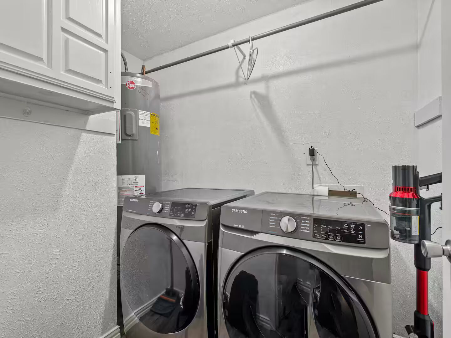 Ein Waschraum mit zwei Samsung Waschmaschinen mit Frontlader und einem Rheem Warmwasserbereiter.