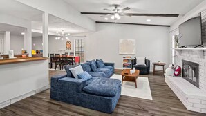 A spacious living room with a sectional sofa, a fireplace, and a dining area in the background. - 4BR Home w/ Arcade, Foosball & Desks - Carrollton (Carrollton)