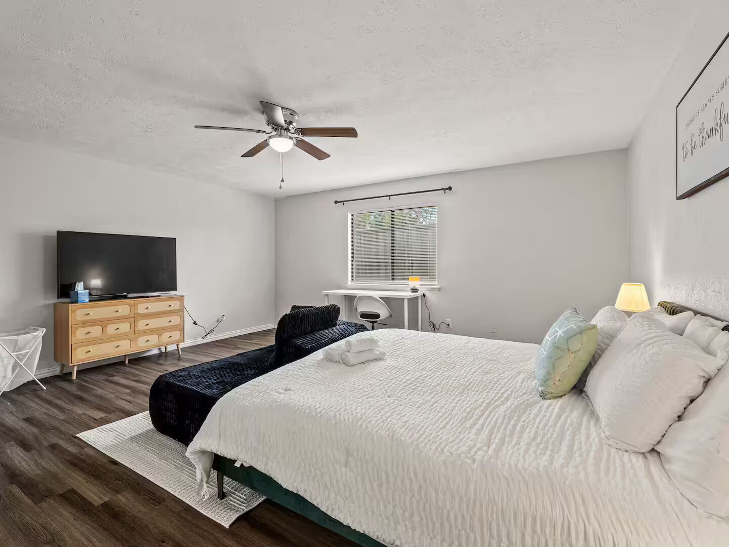 Une chambre à coucher comprenant un lit, un bureau, une télévision et un ventilateur de plafond.