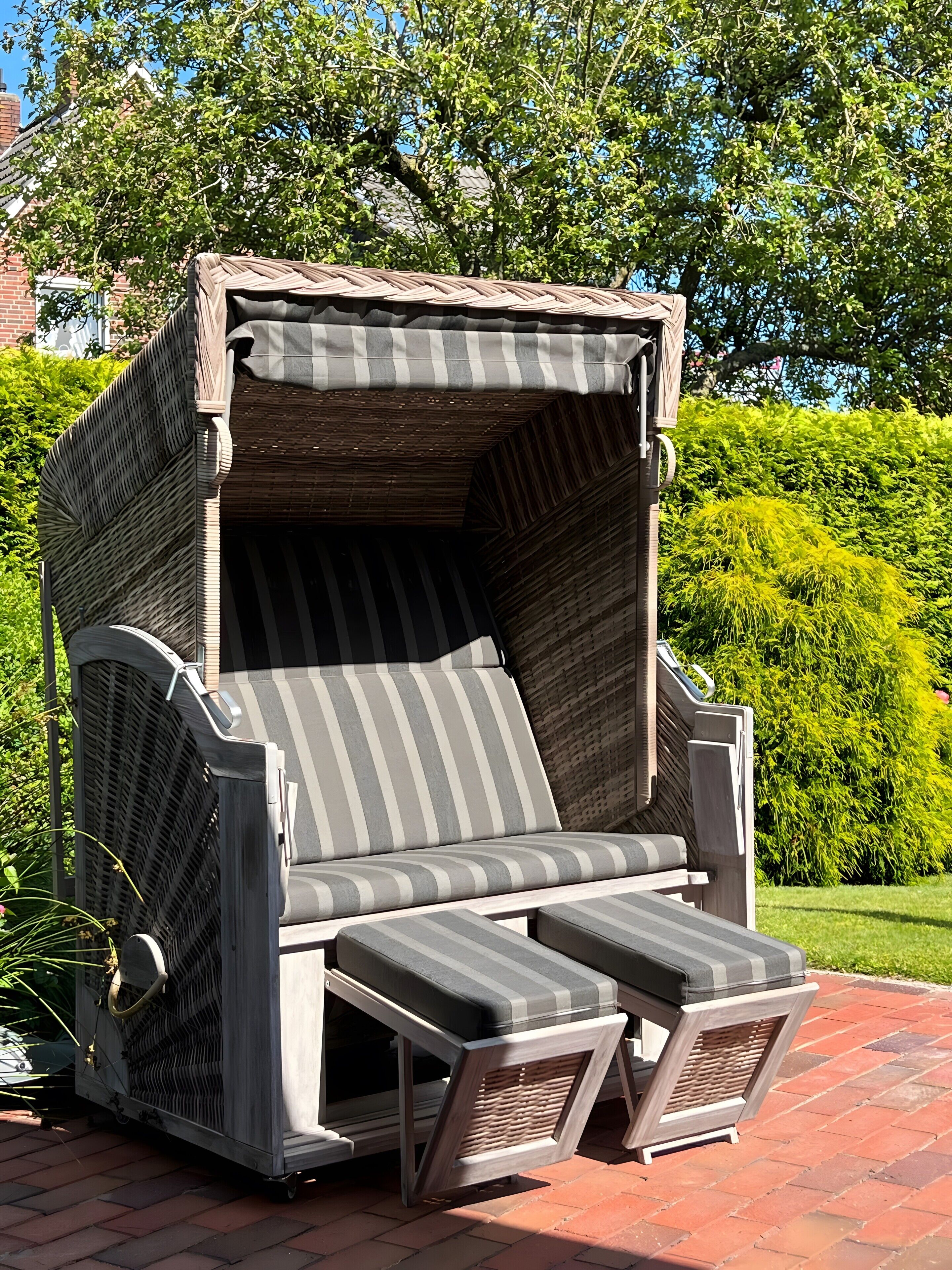 A covered outdoor seating area with a cushioned bench and two attached footrests.