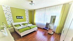 Quarto com cama, mesa de cabeceira, abajur, cadeira e janela com cortinas.