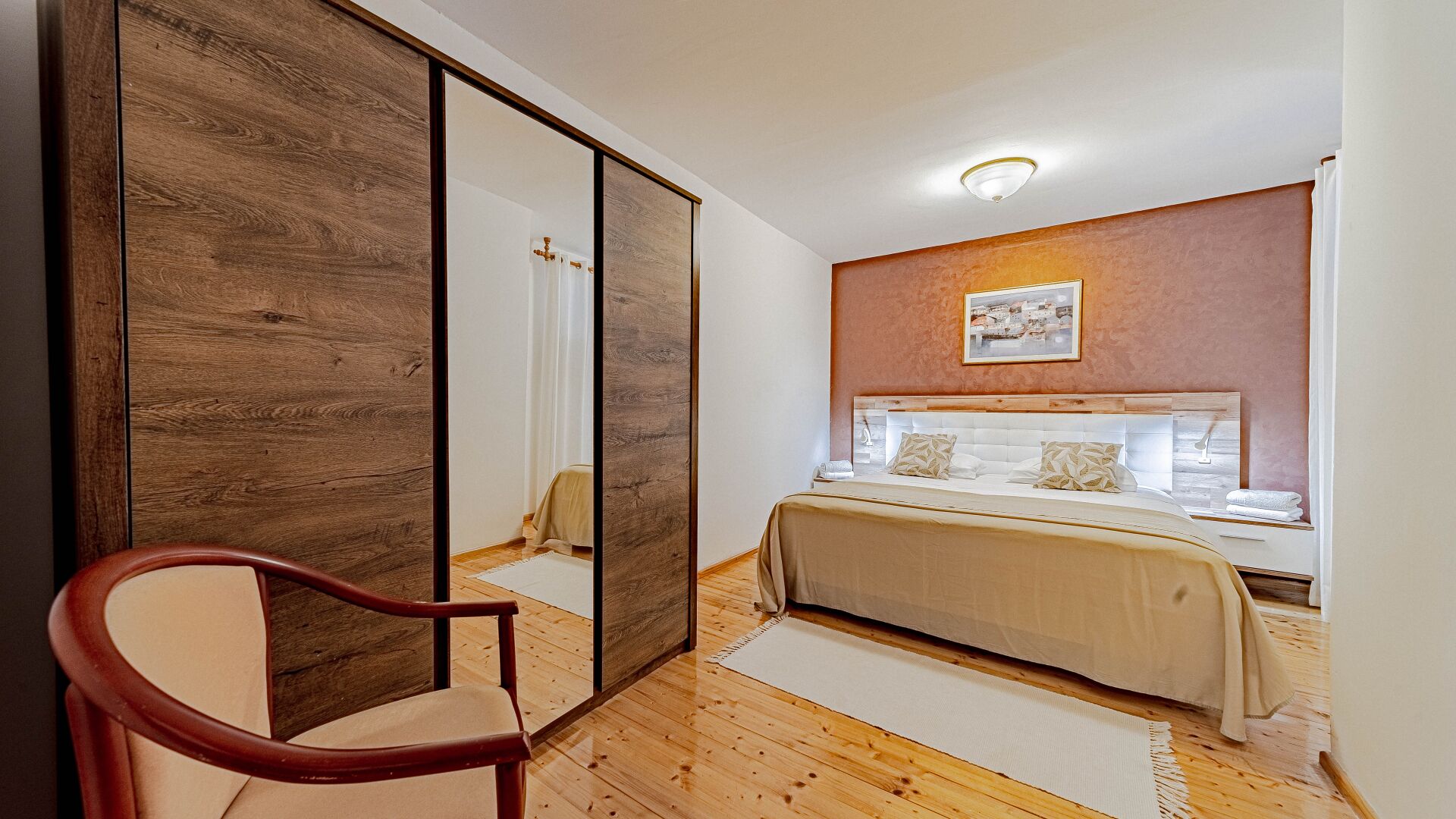 Een slaapkamer met een bed, een stoel, een spiegel en een schilderij aan de muur.