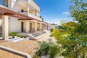 Une maison moderne à deux étages, dotée d’un espace extérieur aménagé et couvert, ainsi que d’une piscine.