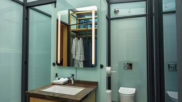 Un baño moderno con cabina de vidrio, tocador de madera, lavamanos, espejo y retrete.