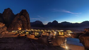 Un resort en el desierto con varias edificaciones iluminadas, terreno rocoso y cielo nocturno despejado.