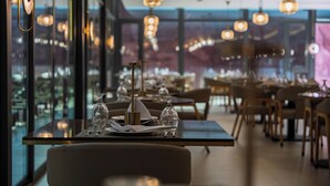 Un restaurante con mesas dispuestas para comer, ventanas amplias y lámparas colgantes.