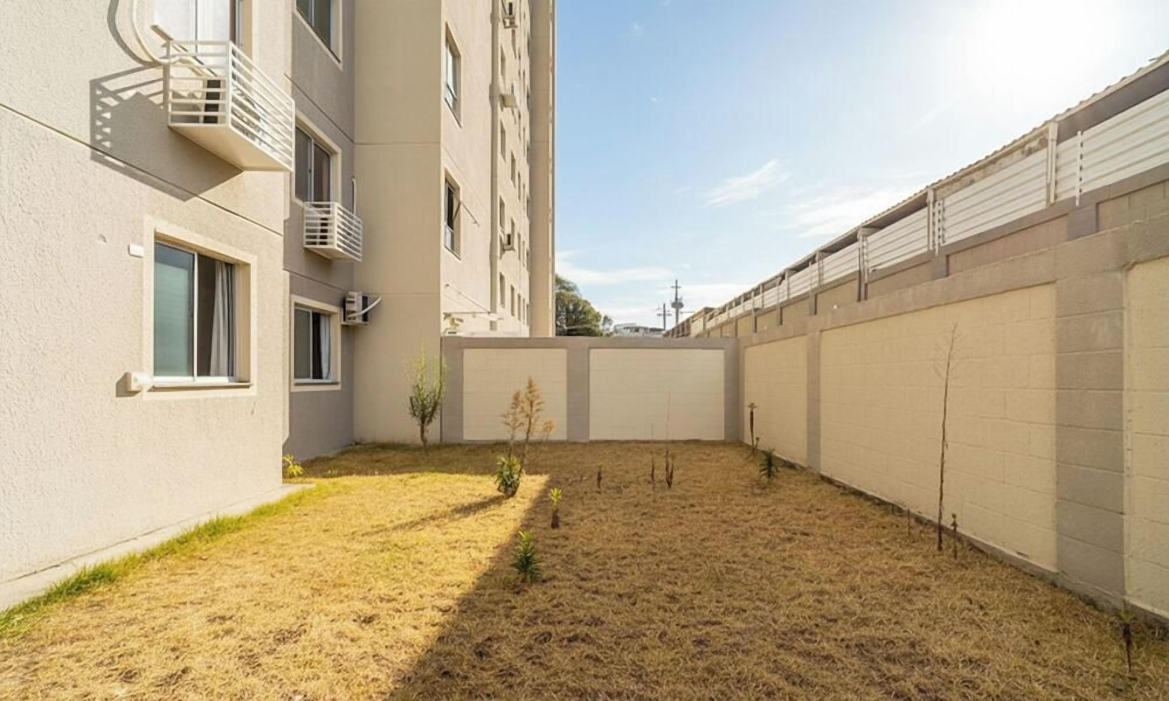 Een binnenplaats met een droog gazon, een kleine boom en een gebouw met balkons en ramen.
