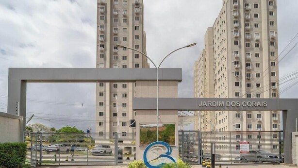 Une entrée sécurisée donnant accès à un complexe résidentiel appelé « JARDIM DOS CORAIS », avec de grands immeubles d’appartements en arrière-plan.