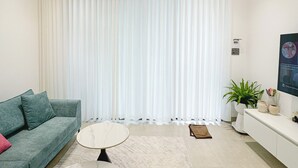 Un salon moderne avec un canapé, une table basse ronde, un ventilateur de plafond et une grande fenêtre équipée de stores verticaux.
