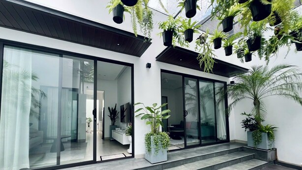 Un bâtiment moderne doté de grandes portes vitrées, d’un escalier menant à un balcon et de plantes en pot, à l’intérieur comme à l’extérieur.