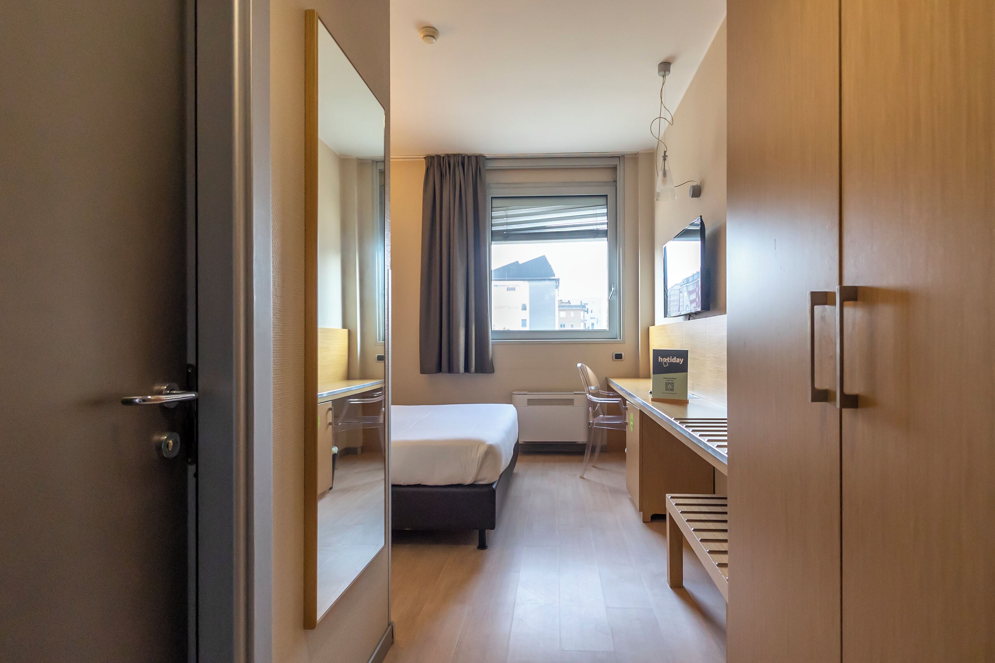 Une chambre d’hôtel avec un lit, un bureau, une chaise et un grand miroir.