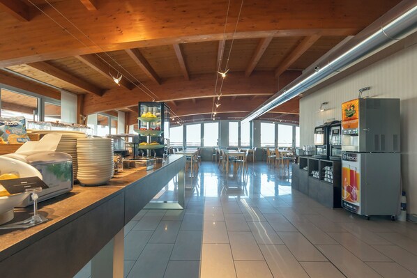 A spacious kitchen with wooden beams, a long counter with various food items, and a refrigerator with a beverage dispenser. - Hotiday Milano Navigli (Milan)