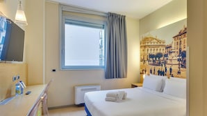 Una habitación de hotel con cama, escritorio, televisión, ventana con cortinas y un mural en la pared.