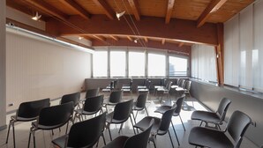 A conference room with rows of chairs, wooden ceiling beams, and large windows. - Hotiday Milano Navigli (Milan)