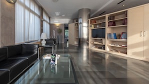 Una biblioteca moderna con una mesa de centro de vidrio, un sofá de cuero negro y estanterías.