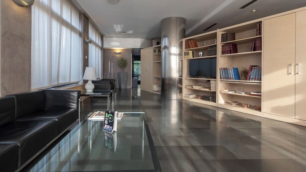 A modern library with a glass coffee table, black leather sofa, and bookshelves. - Hotiday Milano Navigli (Milan)