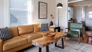 A living room with a leather sofa, a wooden coffee table, a green armchair, and a framed artwork on the wall. - Charming 1901 Home, Modern Updates, Near Lake Superior (Duluth)