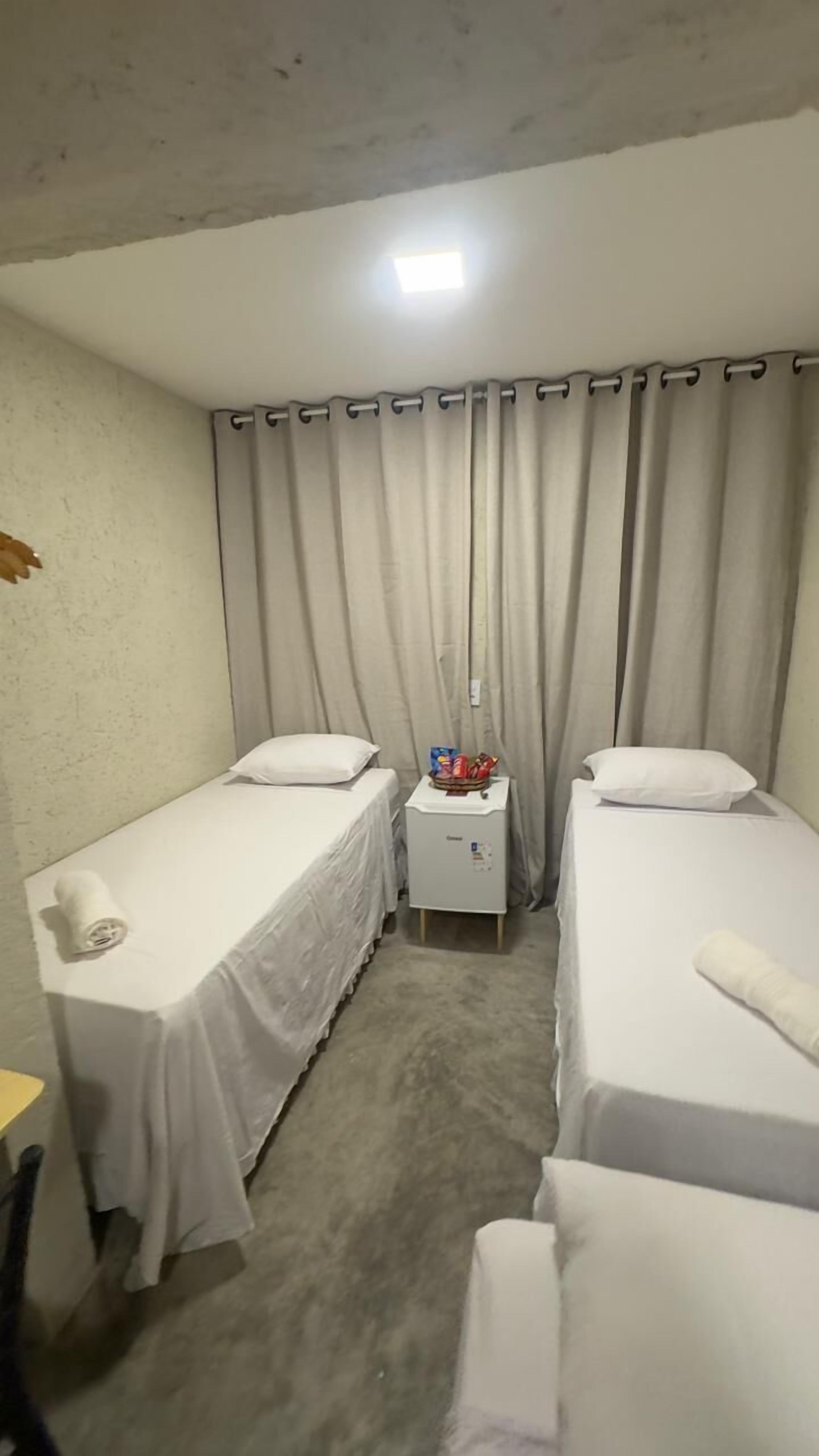 Ein kleines Hotelzimmer mit zwei Einzelbetten, einem kleinen Tisch mit Snacks und einem Vorhang.