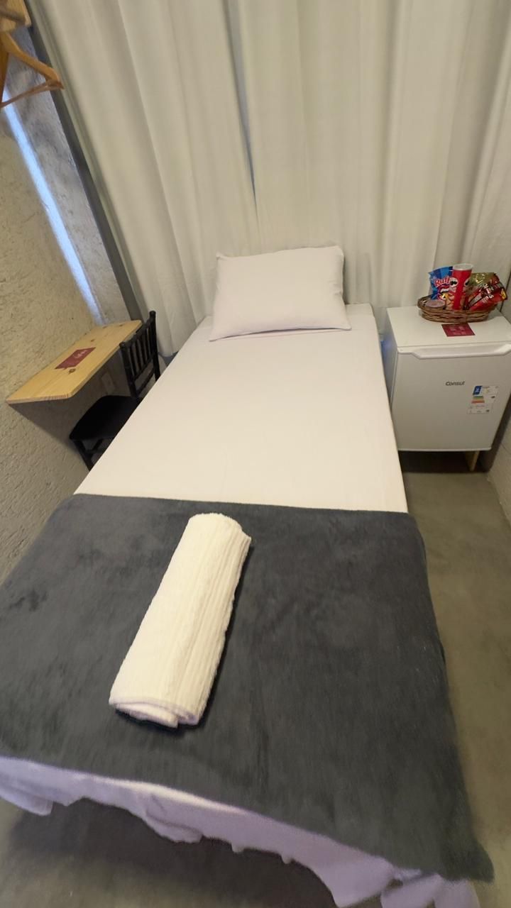 A hotel room with a bed, a bedside table with a basket of snacks, a small heater, and a suitcase on the floor.