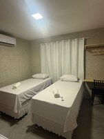 Habitación individual con dos camas individuales, una mesita, una silla, perchero y aire acondicionado.
