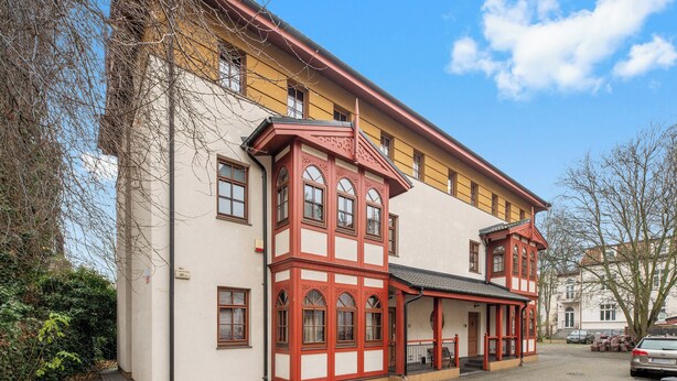 A two-story building with a red and white facade, a covered porch, and a paved driveway. - Zacisze Centrum 2 9 12byGrand Apartments (Sopot)