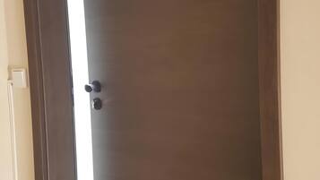 Eine geschlossene, dunkelholzige Tür mit Griff, Lichtschalter und Steckdose an der linken Wand.