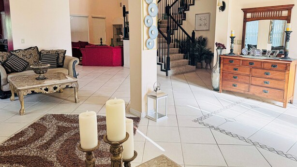 Een ruime woonkamer met een bank, salontafel en een open haard. Een trap leidt naar een verdieping boven, en in de achtergrond staat een houten dressoir.