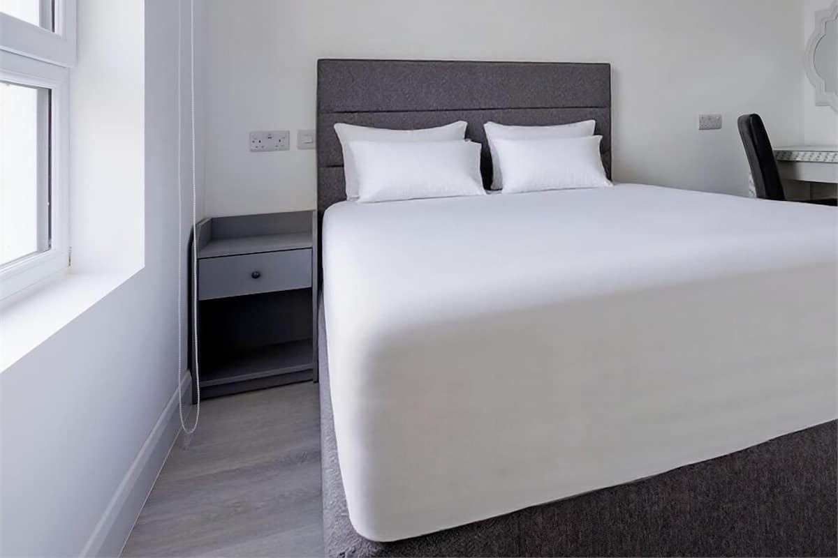 A modern hotel room with a large bed, a nightstand, and a window.