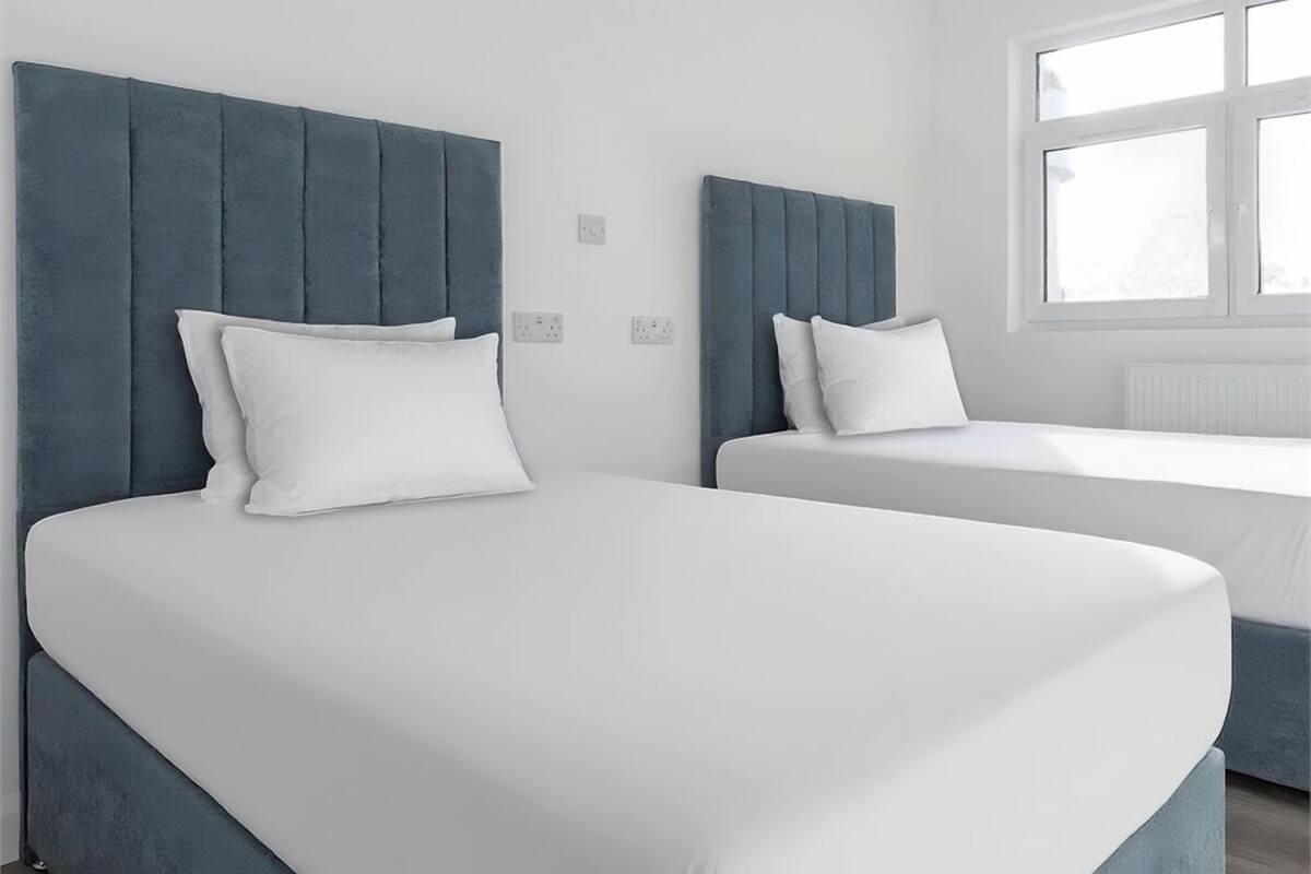 A modern hotel room with two beds, a large window, and a white wall.