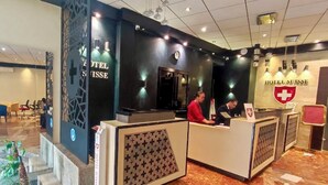A hotel reception area with a modern design, featuring a reception desk, a clock, and a logo with a cross. - Suisse Hotel - Alger Centre (Algiers)