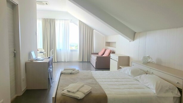 Een moderne hotelkamer met een groot bed, een bureau met een laptop, een stoel en uitzicht op het landschap door grote ramen.