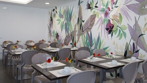 Een eetgedeelte met tafels voor vier personen, elk met een witte tafelkleed, bestek en een vaas met bloemen.