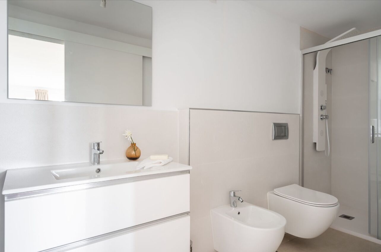Une salle de bain moderne avec un grand miroir, un lavabo blanc, un bidet et une douche.