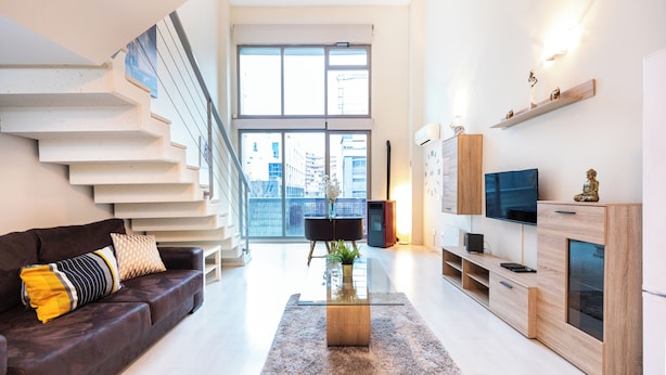 A modern living room with a staircase, a sofa, a coffee table, and a TV stand.