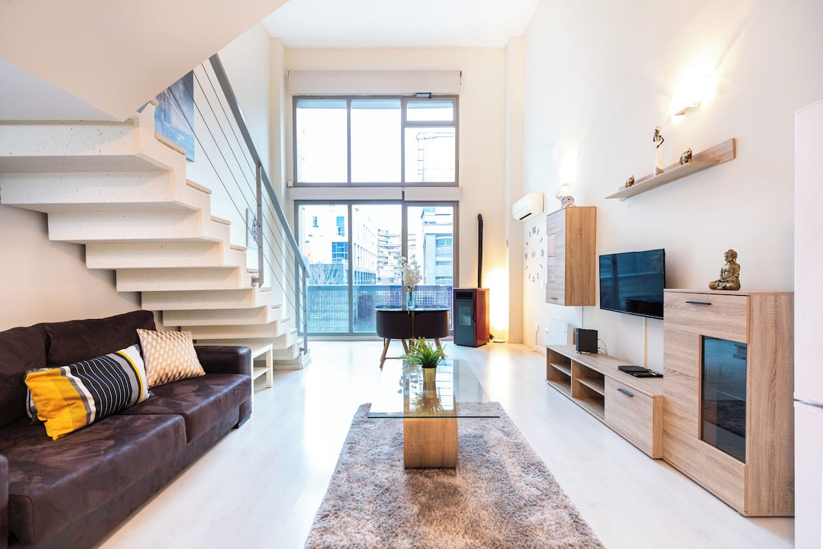 A modern living room with a staircase, a sofa, a coffee table, and a TV stand.