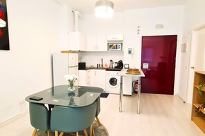 Cocina compacta con microondas, pileta y lavadora. Hay una mesa de vidrio con sillas y un florero con flores.